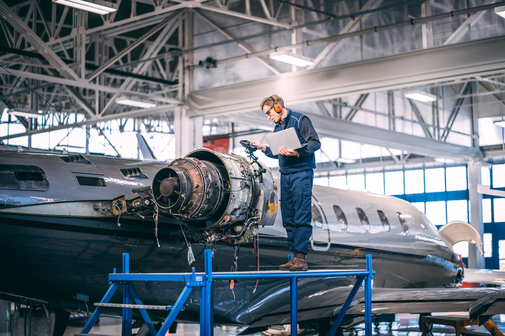 Aircraft engineer standing on a raised work platform, looking at a display of a probe inspection camera, trying to diagnose a fault in a jet engine of a small private airplane in a maintenance hangar